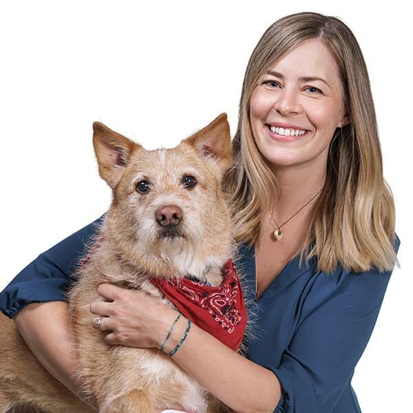 Board-Certified Veterinary Oncologist and Medical Director, Lisbeth (Liz) Ambrosius, hugging her fluffy brown pet dog.