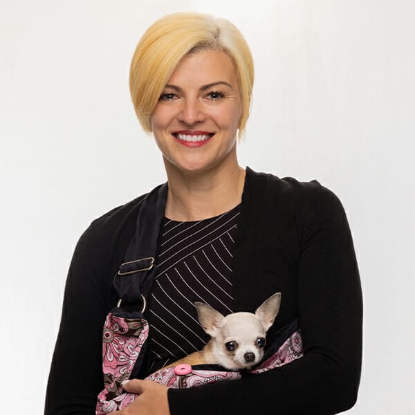 Board-certified Specialist in Veterinary Anesthesia & Analgesia and Medical Director, Dr. Carrie Davis, holding her tiny white pet dog in a pink sling and smiling