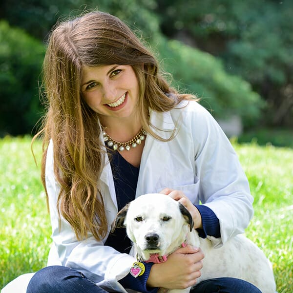 Medical Director of MedVet Hilliard, Dr. Mackenzie Ruehl, hugging her small white pet dog and smiling in a green field