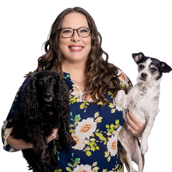 Hospital Director, Jennifer Laessig, smiling while wearing a bright blue shirt and holding her two pet dogs