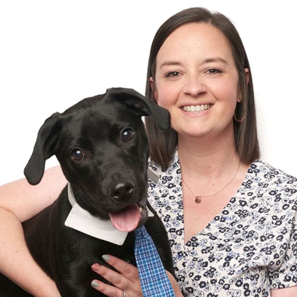 Hospital Director, Kayla Edwards, smiling while wearing a bright white shirt and hugging her black pet puppy who is wearing a blue tie