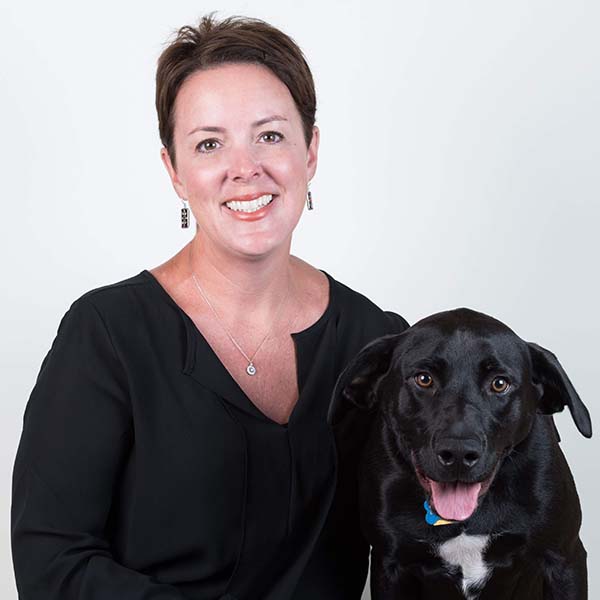 Dr. Kristin Herbert-Fisher, DVM and Medical Director of MedVet Mandeville, smiling in a black shirt while hugging her black and white pet dog