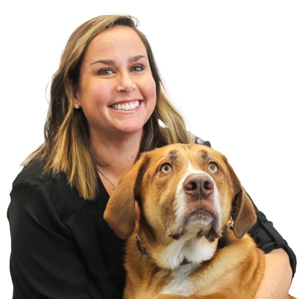Hospital Director, Tara Manganiello, hugging her brown and white pet dog and smiling happily